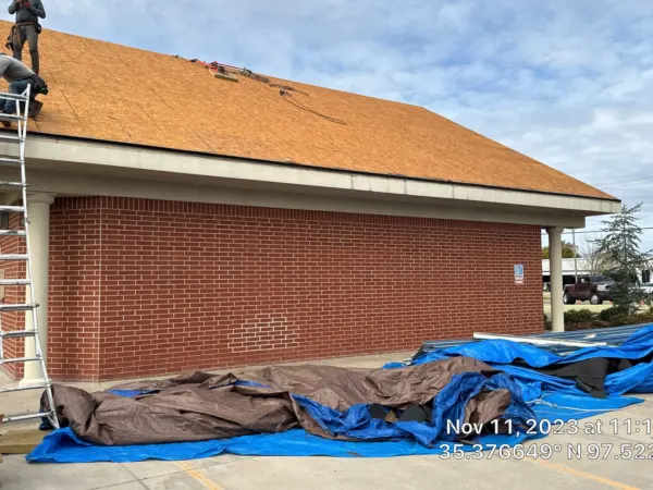 Crew working on the brick commercial building roof with tarps below