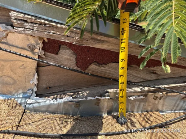 Tape measure showing deteriorated roof edge and decking during inspection