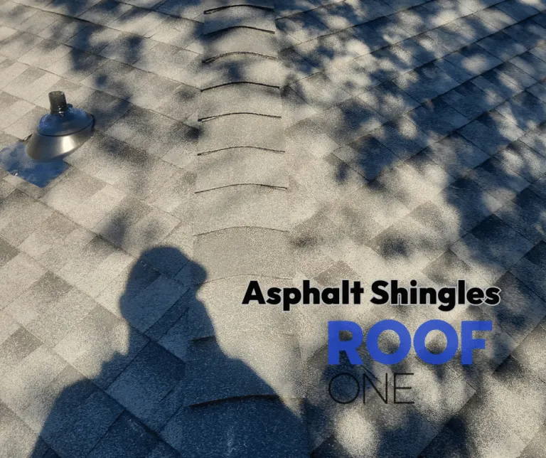 A close-up of a residential roof covered in gray asphalt shingles, showing the ridge line and a plumbing vent.