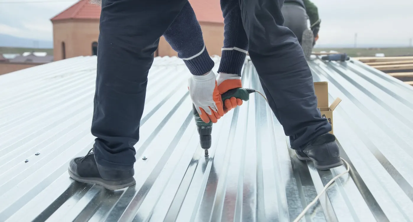 Edmond OK Metal Roof Replacement by Roof One: Contractor using a power drill to secure silver corrugated metal roofing panels.