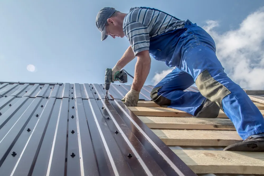 Edmond OK Metal Roof Replacement by Roof One: Roofer installs dark brown metal panels over wooden slats on a sunny day.